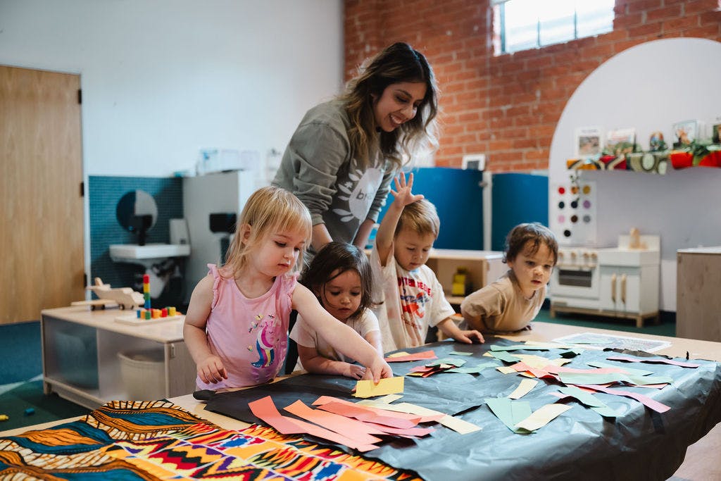 Adult and multiple children doing an art project in a classroom