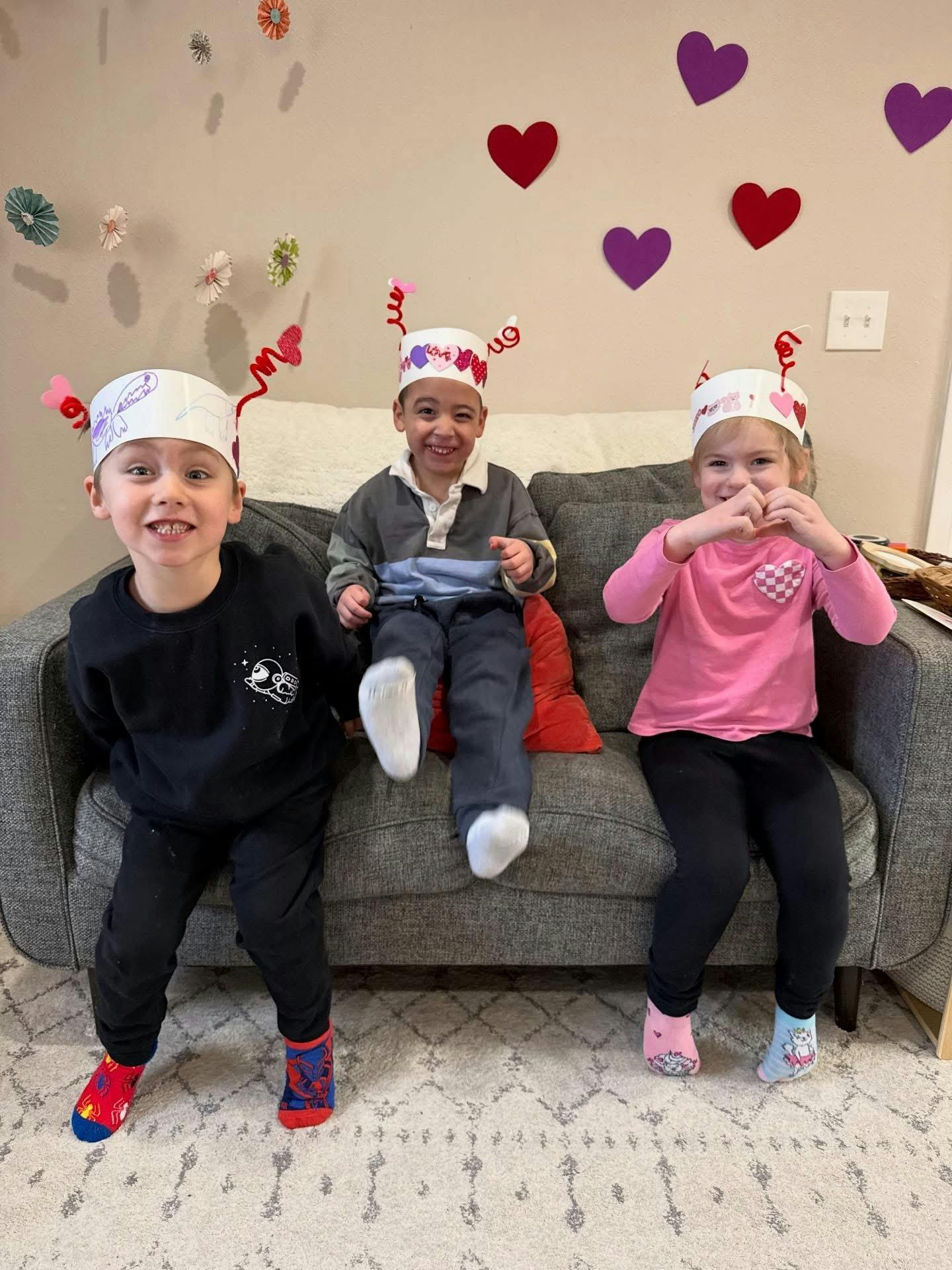 Three children sitting on a couch wearing decorated paper crowns