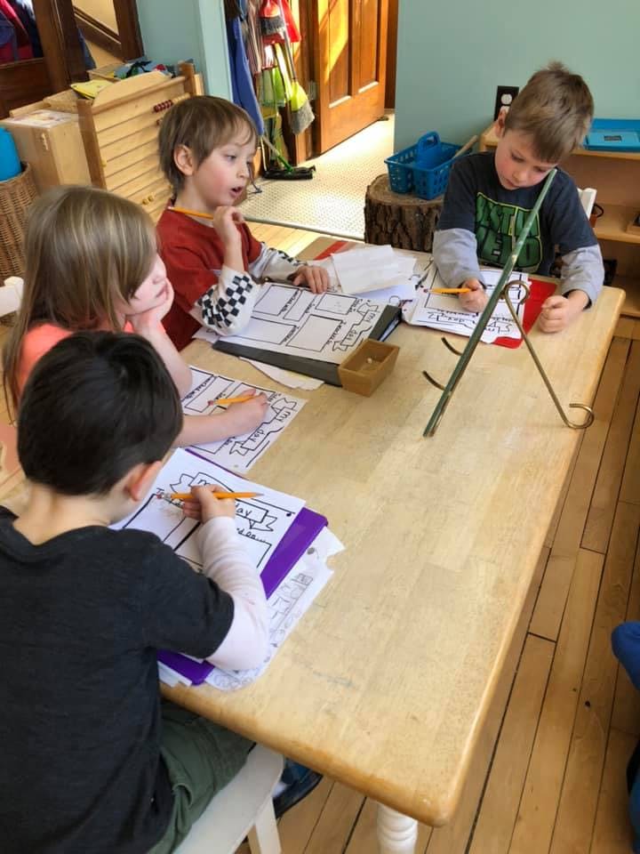 Four children drawing at a table in a classroom