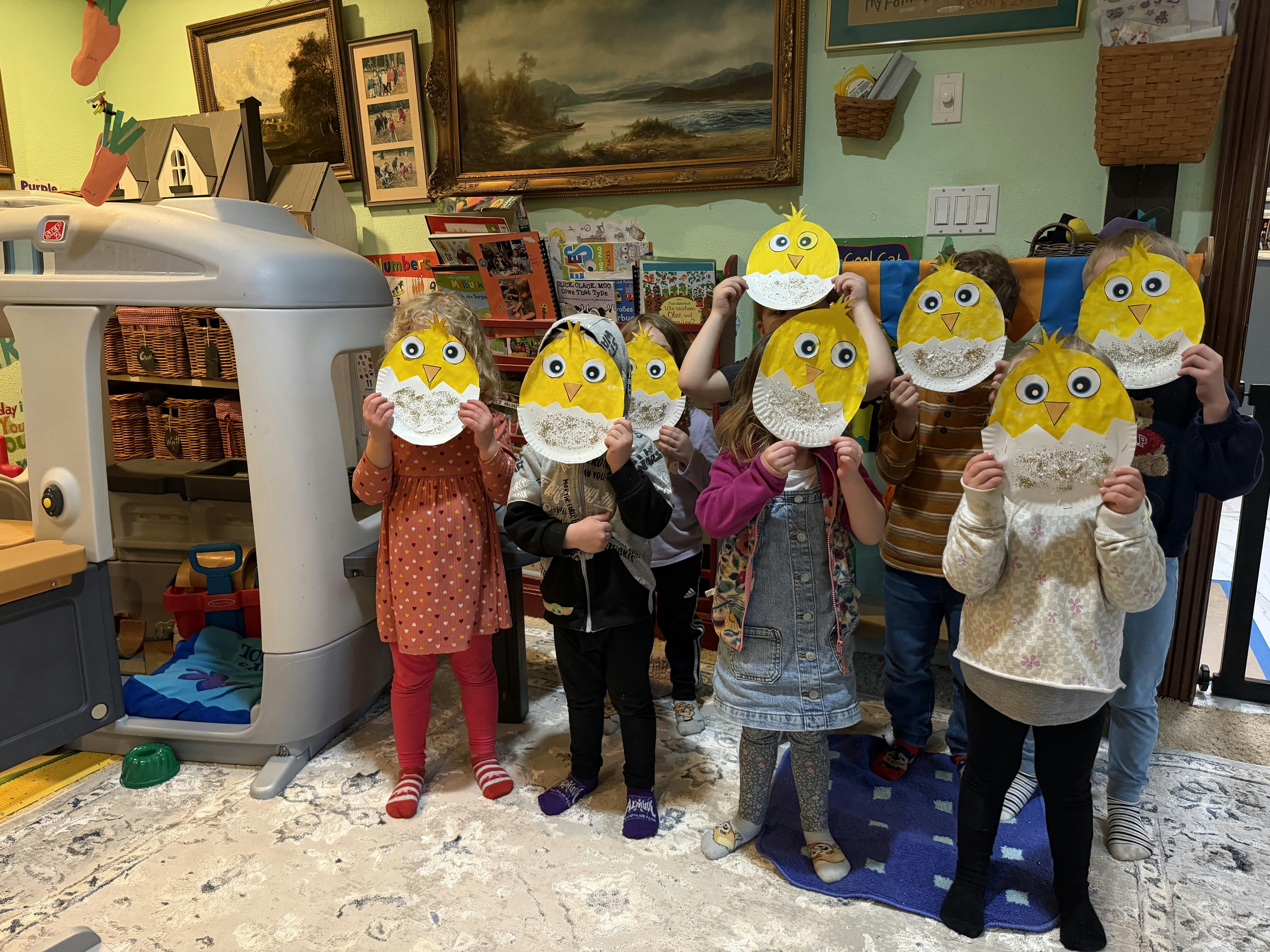 Group of children holding paper chick crafts in front of their faces