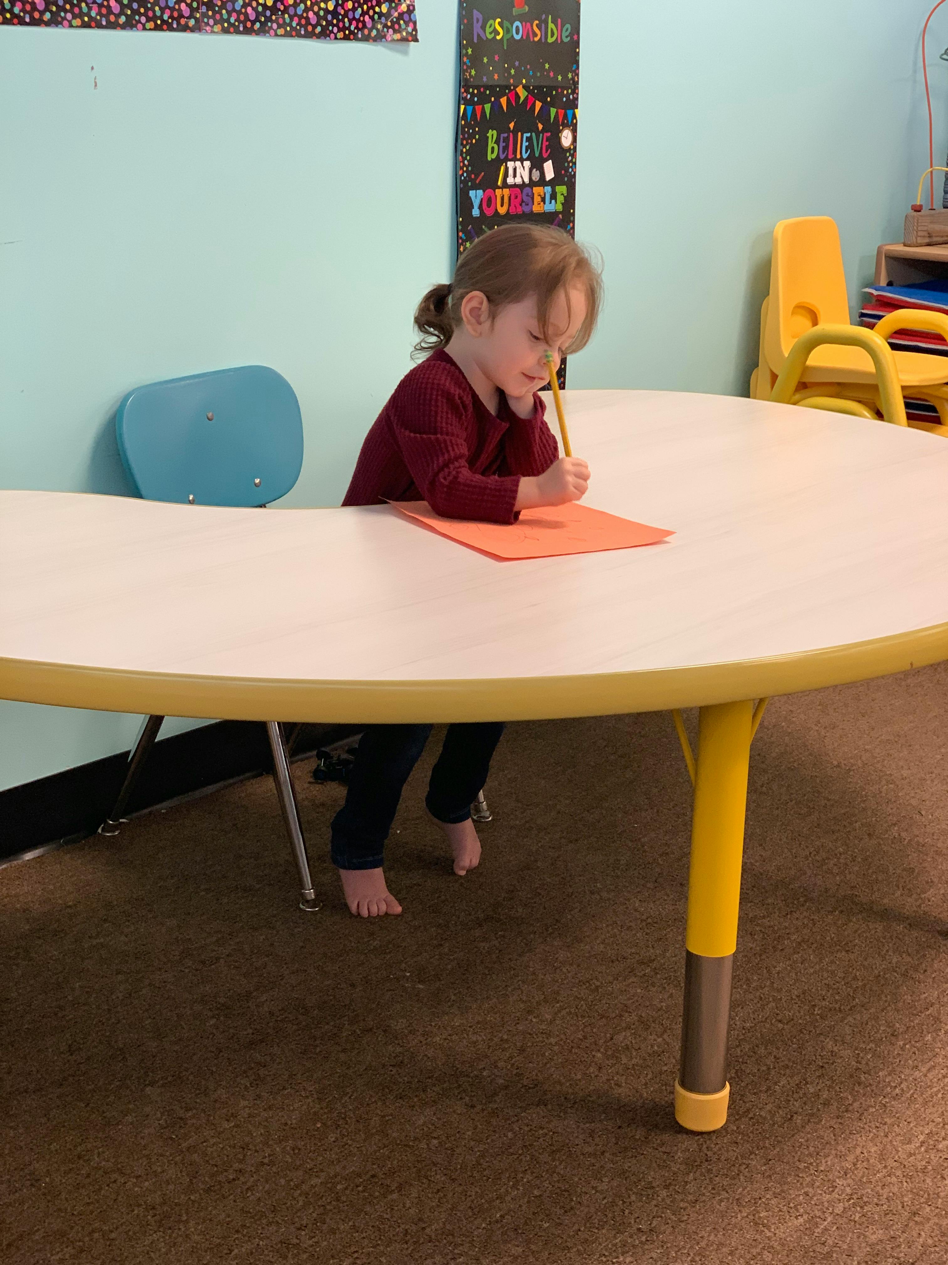 Child writing on orange paper at a table