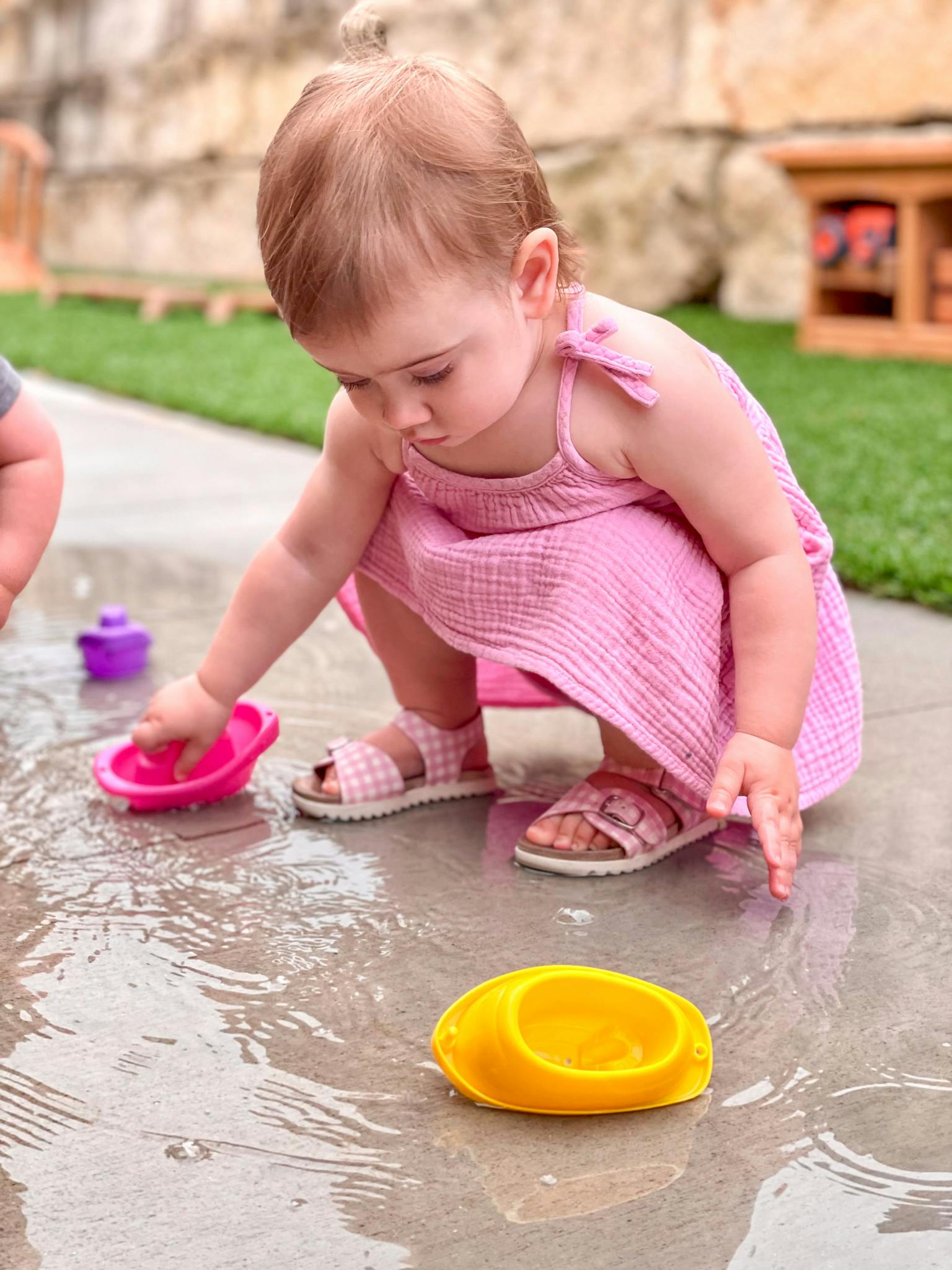 Child playing with toy boats in a puddle