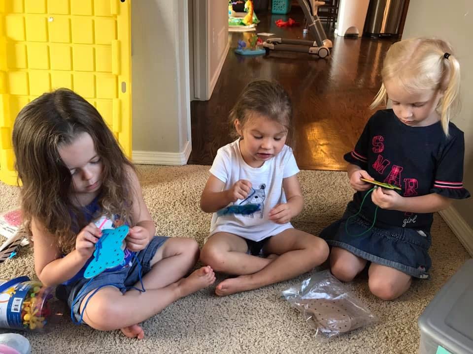 Three children sitting on a rug, engaged in crafts