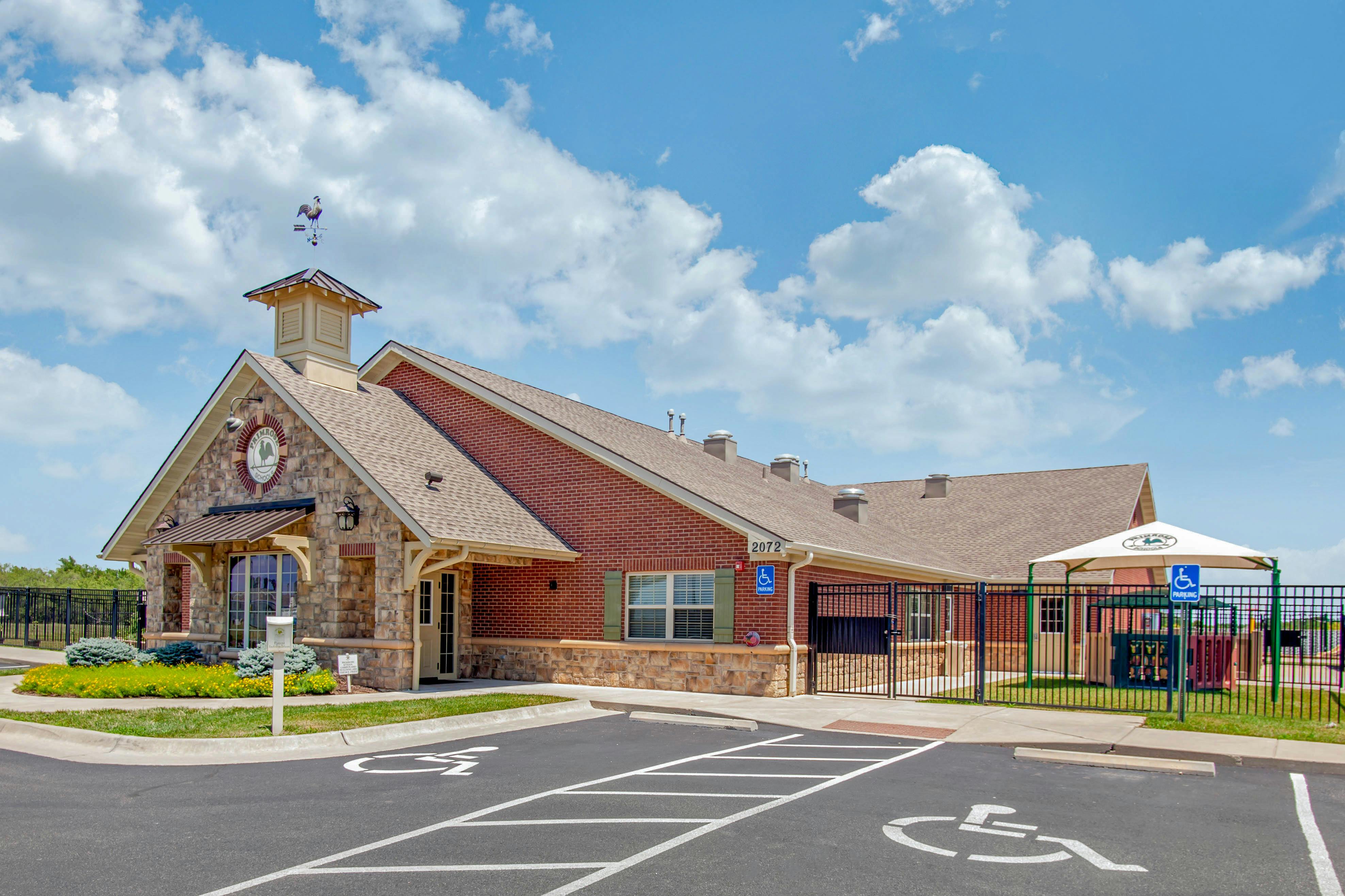 A low-rise building with brick and stone, a steeple, and a parking lot