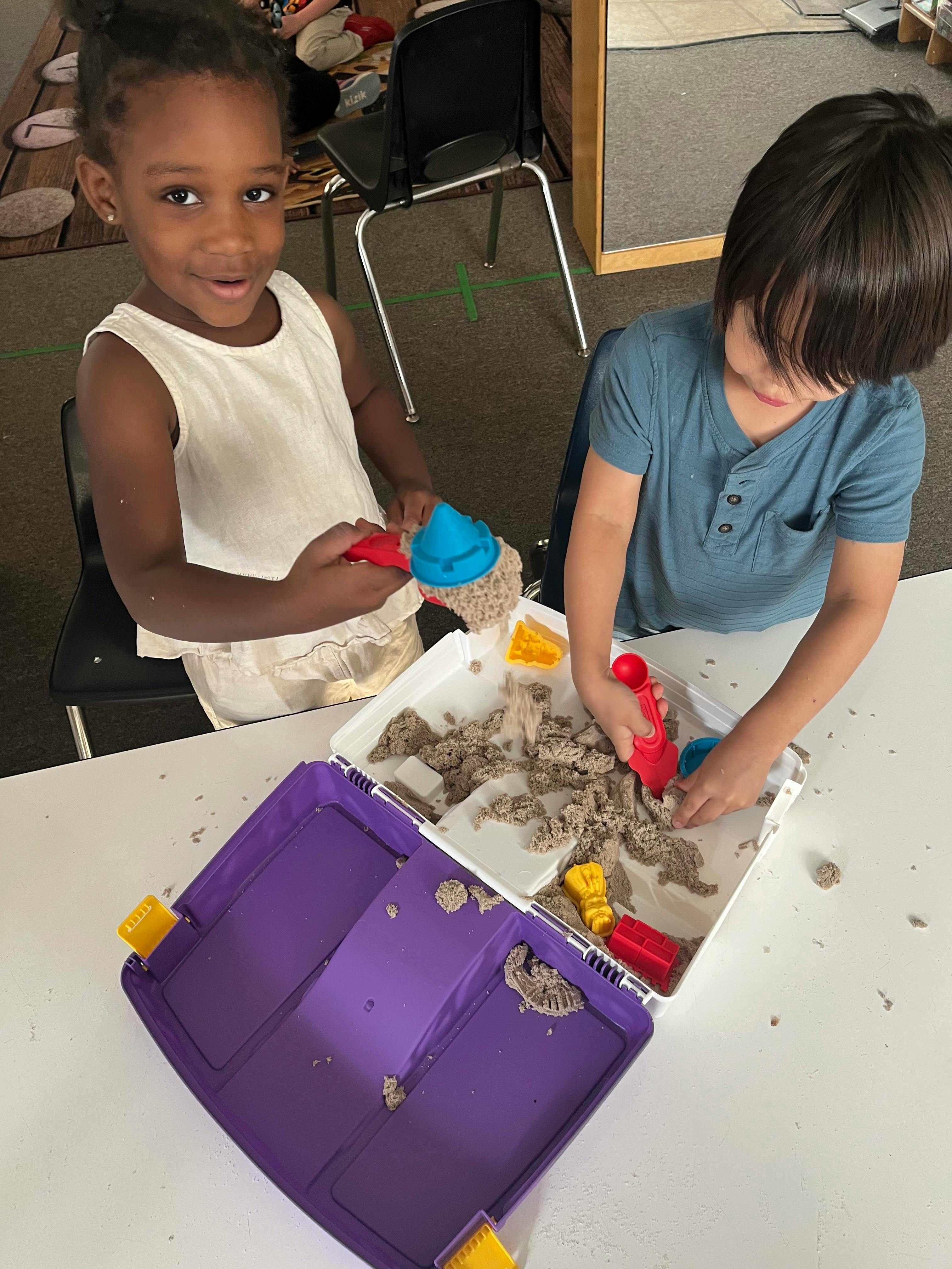Two children playing with kinetic sand and toys