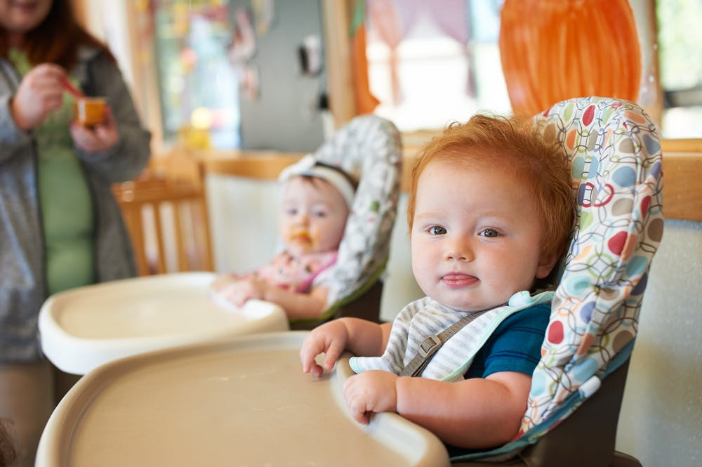 Two children in high chairs, one in foreground looking forward