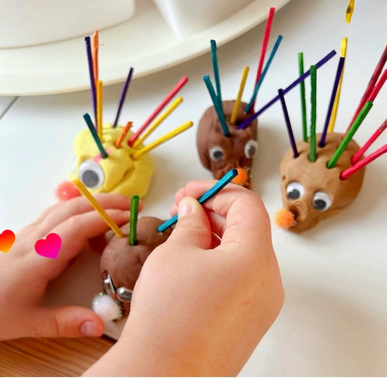 Child crafting playdough figures with googly eyes and colorful sticks