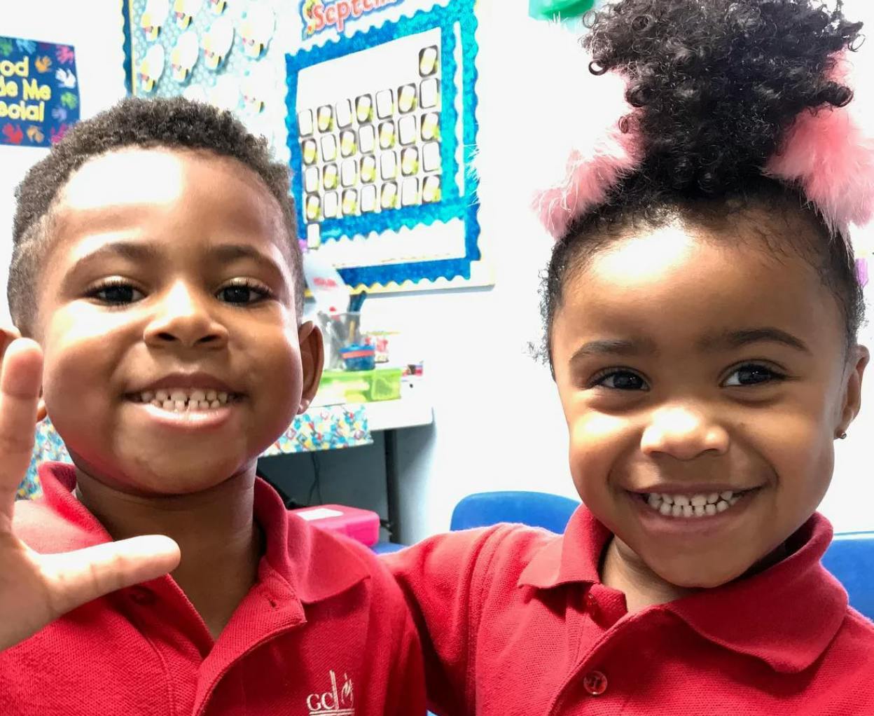 Two children in red shirts smiling in a classroom