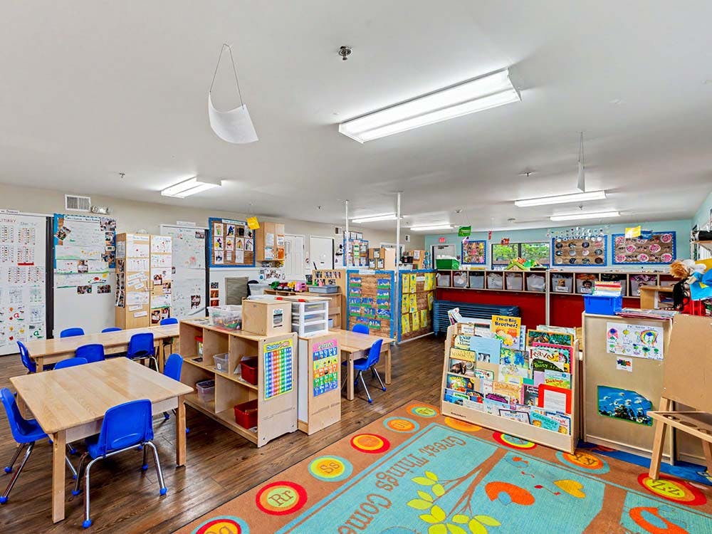 Classroom with small tables, chairs, bookshelves, and colorful rug