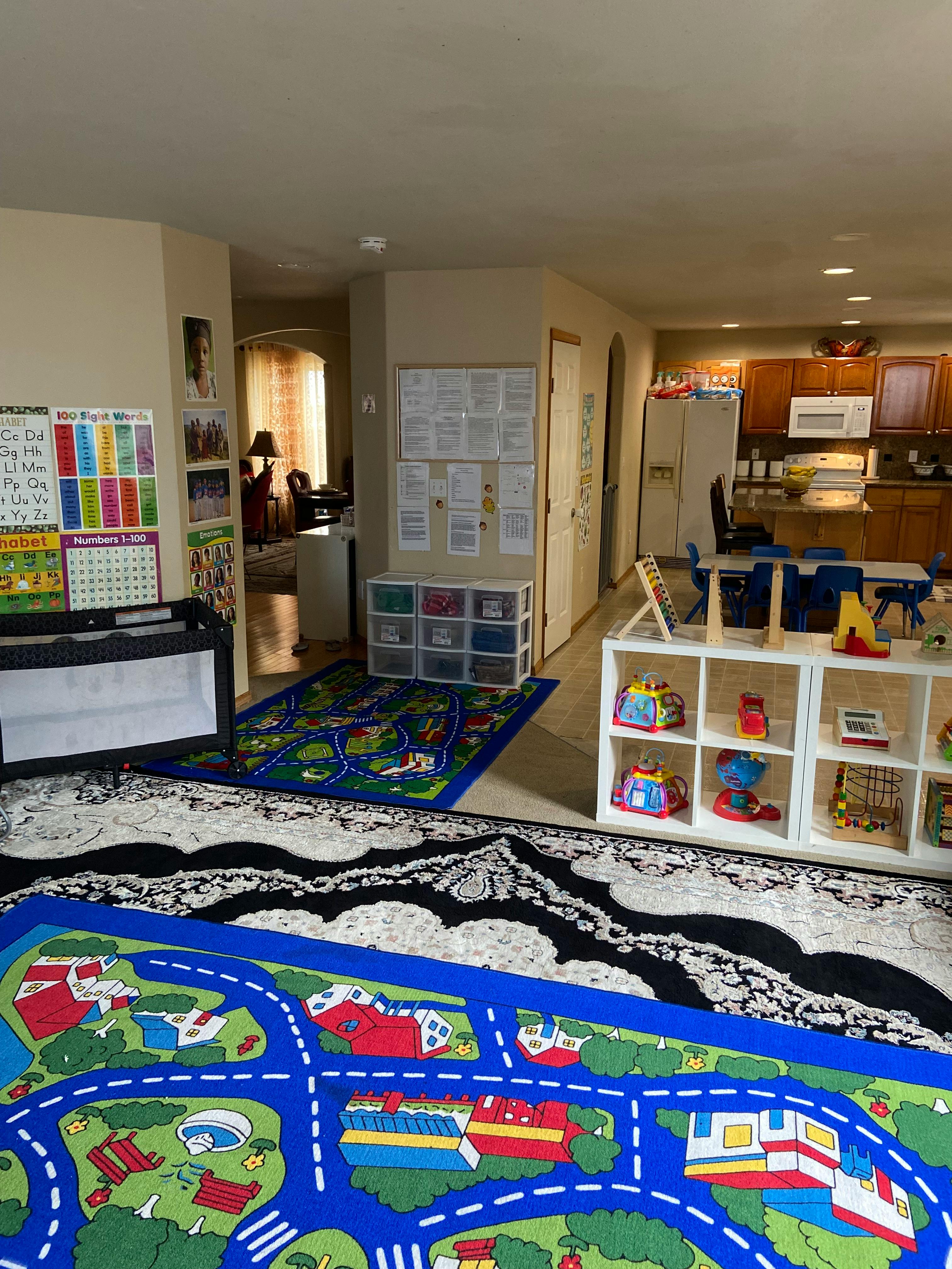 Playroom with colorful rugs, toys, and a view into a kitchen