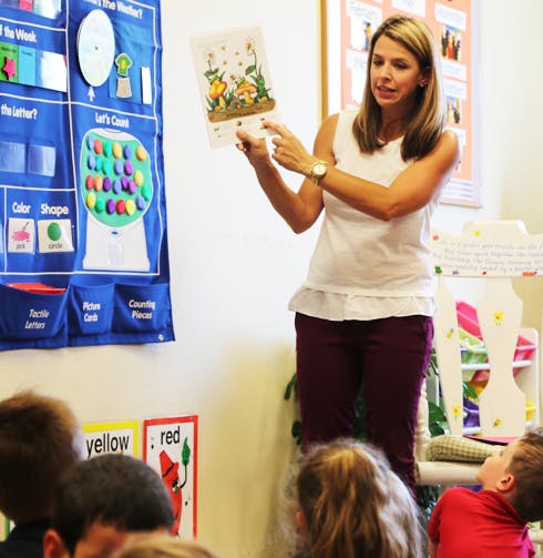 Person holding up and pointing at a picture book in a classroom