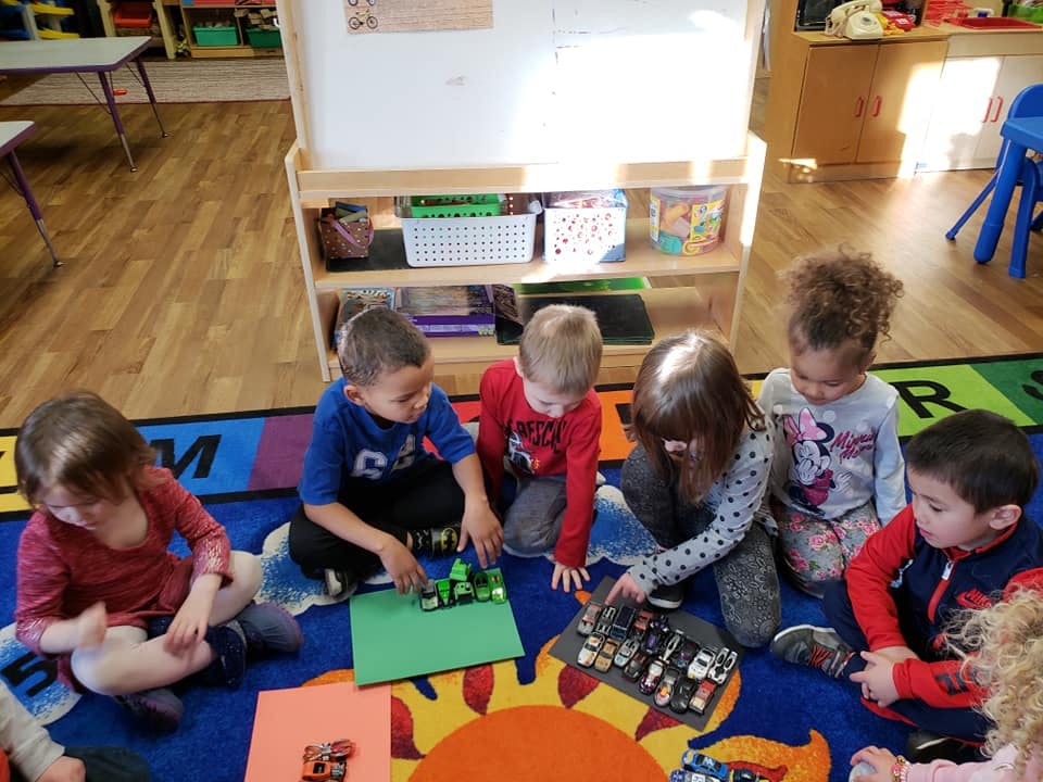 Children playing with toy cars on a rug in a classroom
