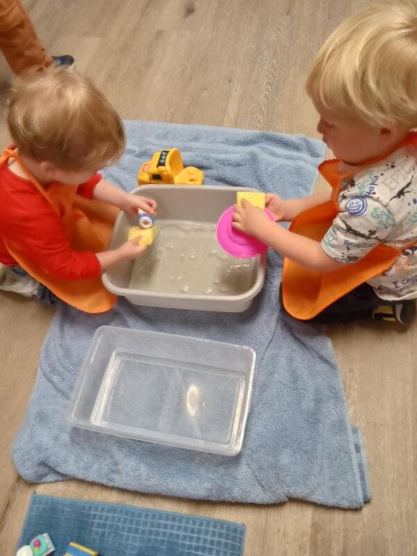 Two children playing with water in a bin