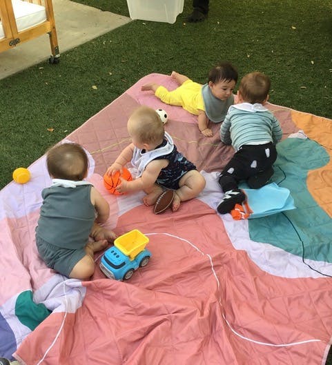 Four children playing with toys on a blanket outdoors