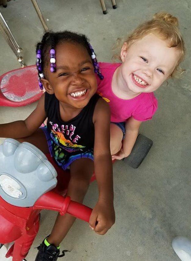 Two children smiling, one on a red ride-on toy