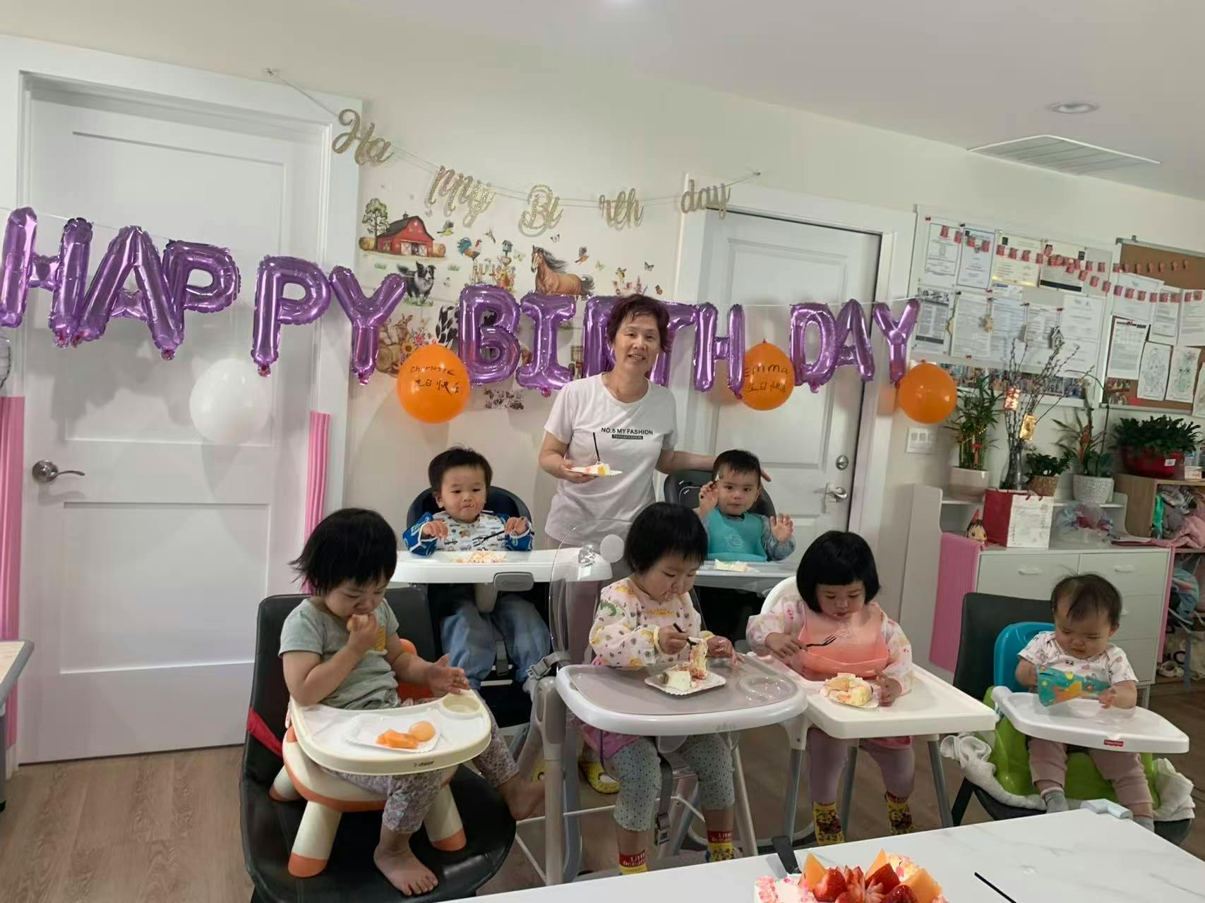 Adult helping children eat cake at a birthday celebration with balloons