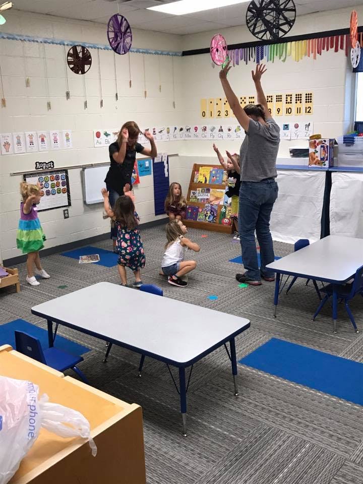 Adults and children in a classroom with arms raised