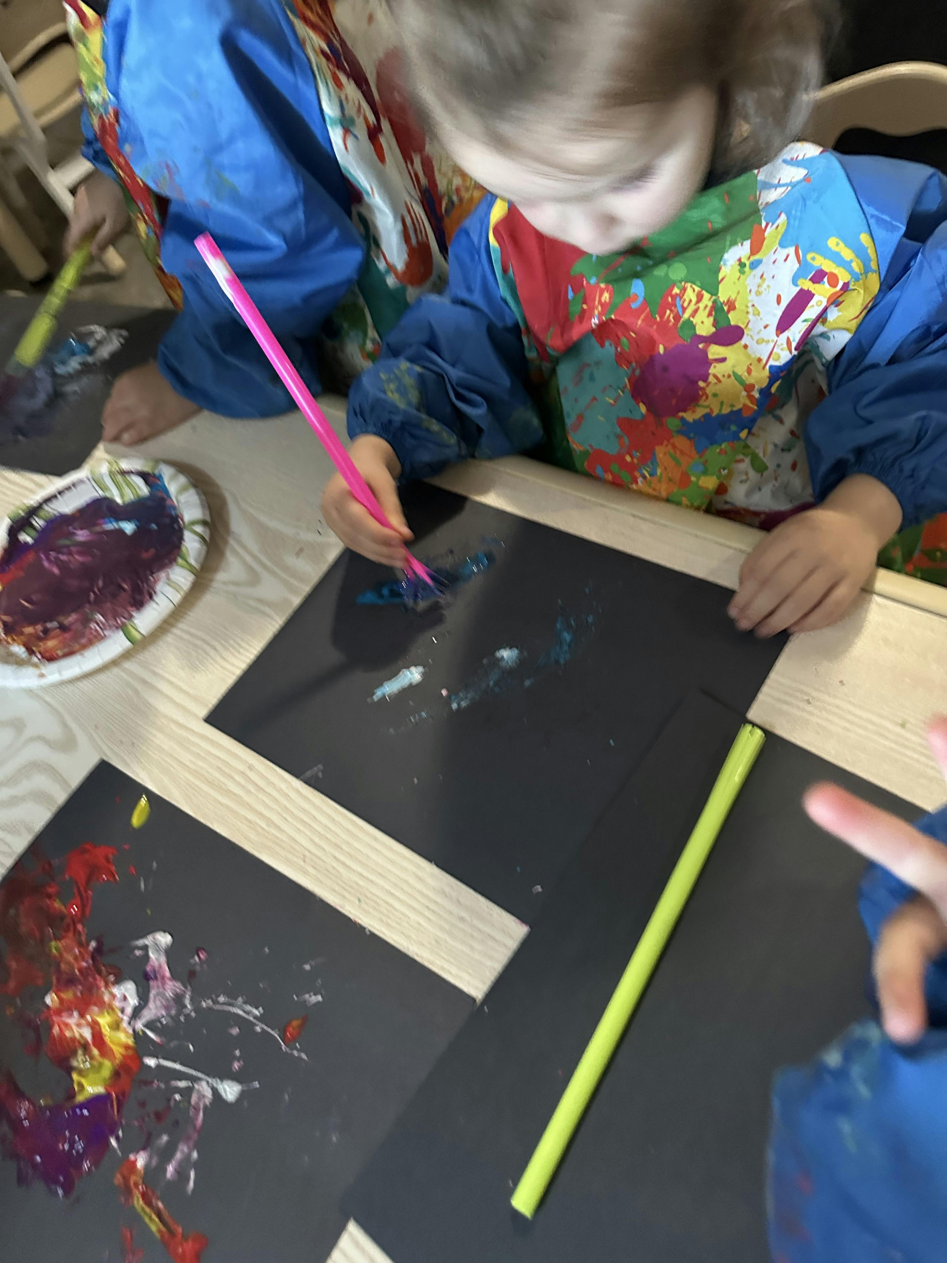 Child wearing a paint smock using a brush on black paper