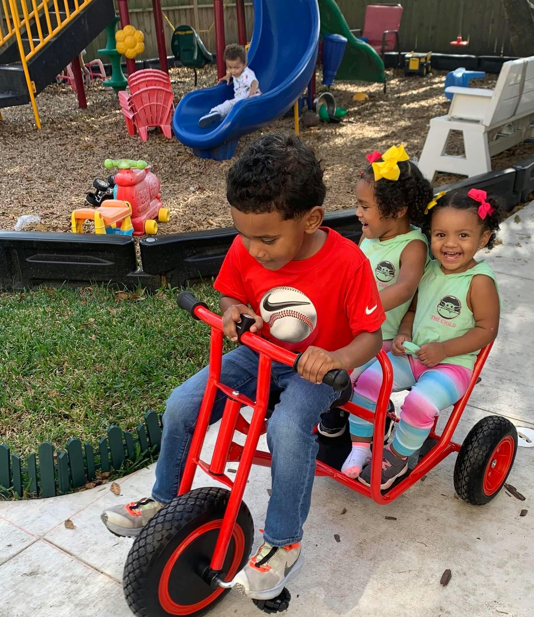 Child on a red tricycle with two children in the back seat