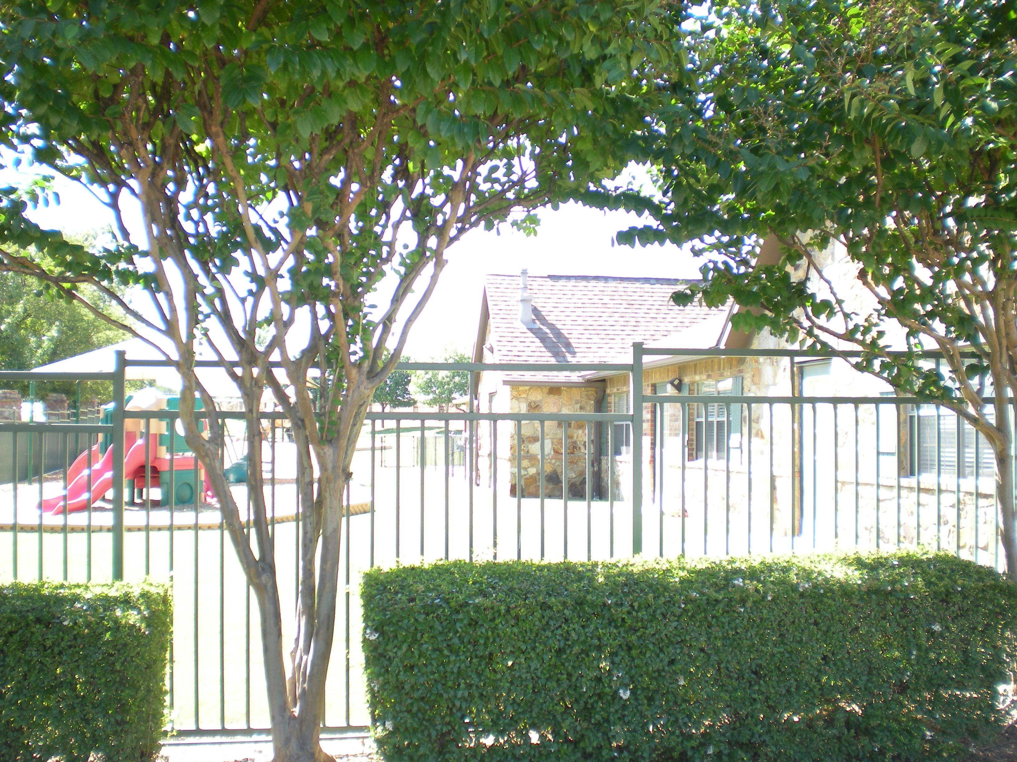 Playground behind a fence and hedge with a building in the background