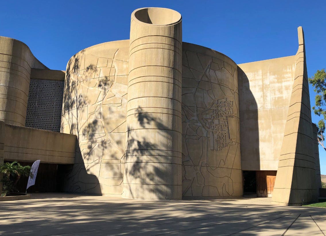 Curved concrete building with a cylindrical tower and tree shadows