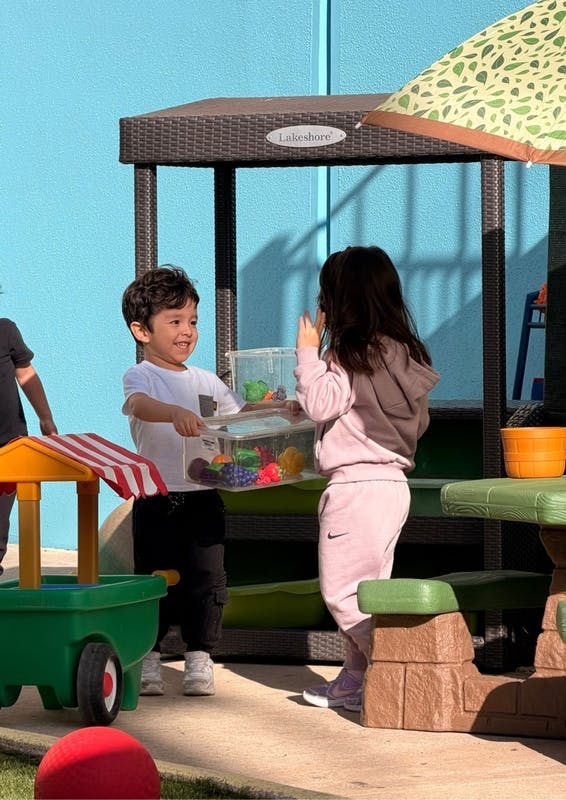 Child giving another child a clear container of toy fruit