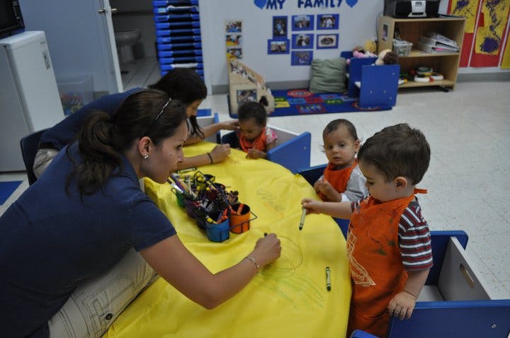 Two people and two children drawing on a yellow surface in a classroom