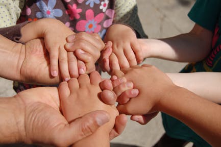 Multiple hands of adults and children holding each other