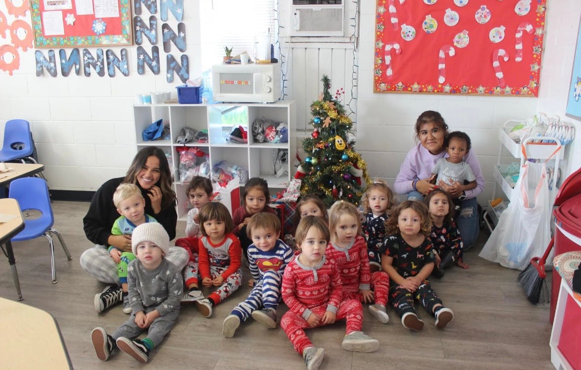 Two people with a group of children sitting on the floor in a classroom