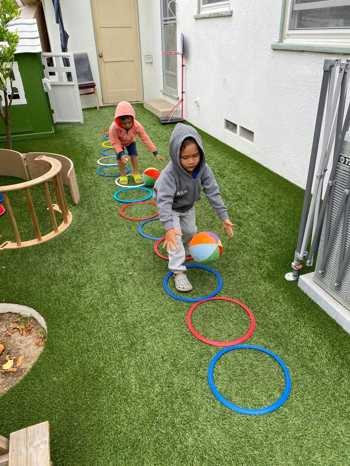 Two children playing with a ball and rings on artificial grass
