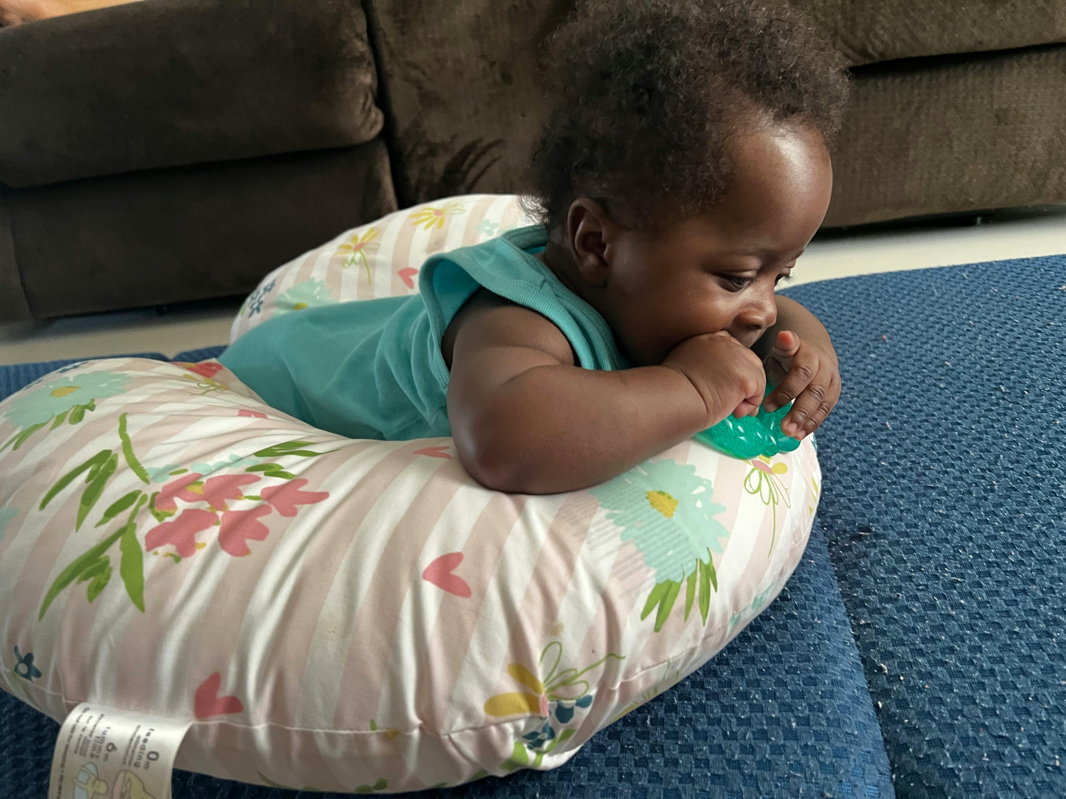 Child on a patterned pillow chewing on a toy