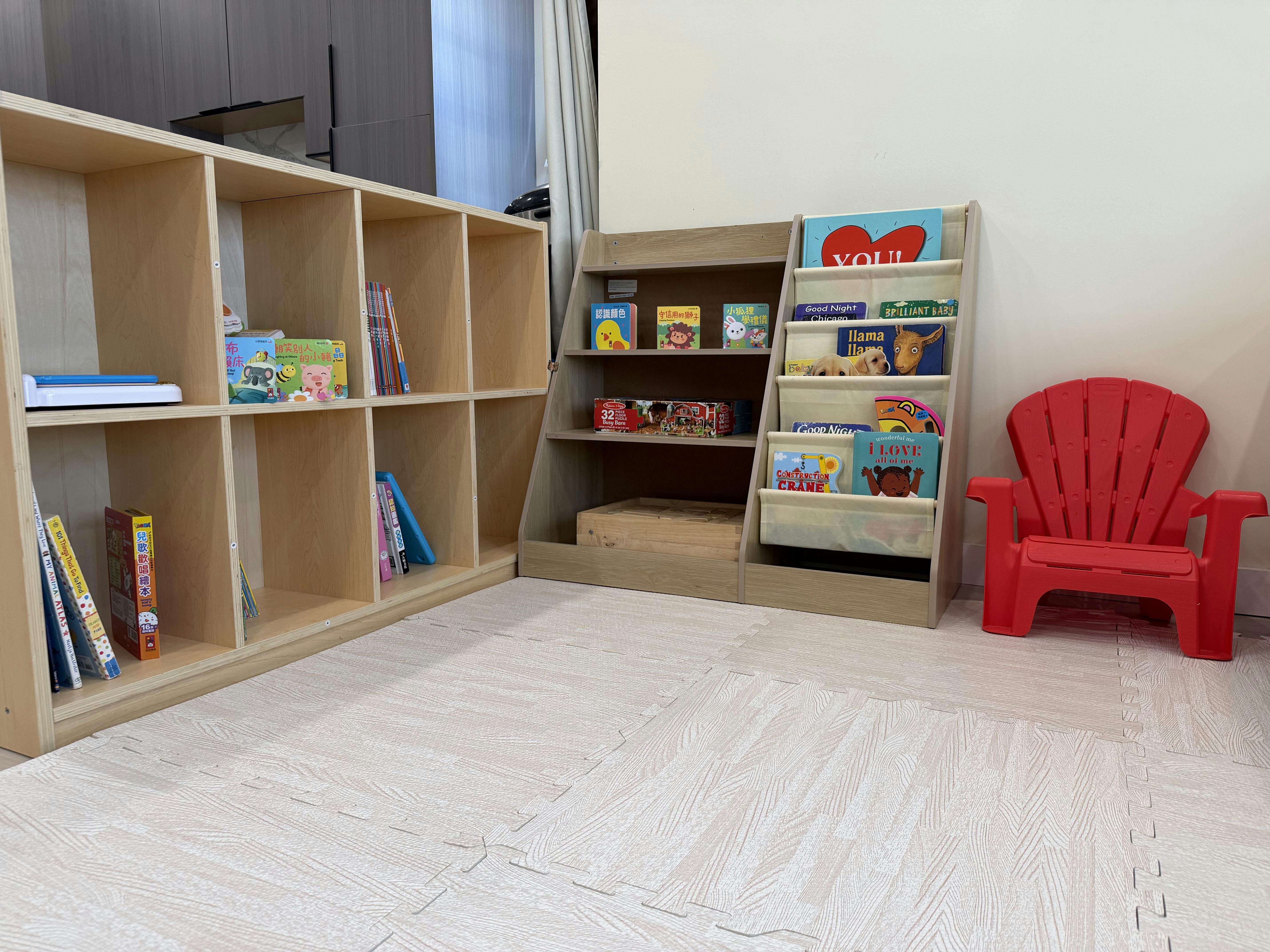 Children's books on two shelves and a red plastic chair on a foam mat