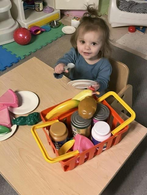 Child sitting at a small table playing with plastic food and a basket