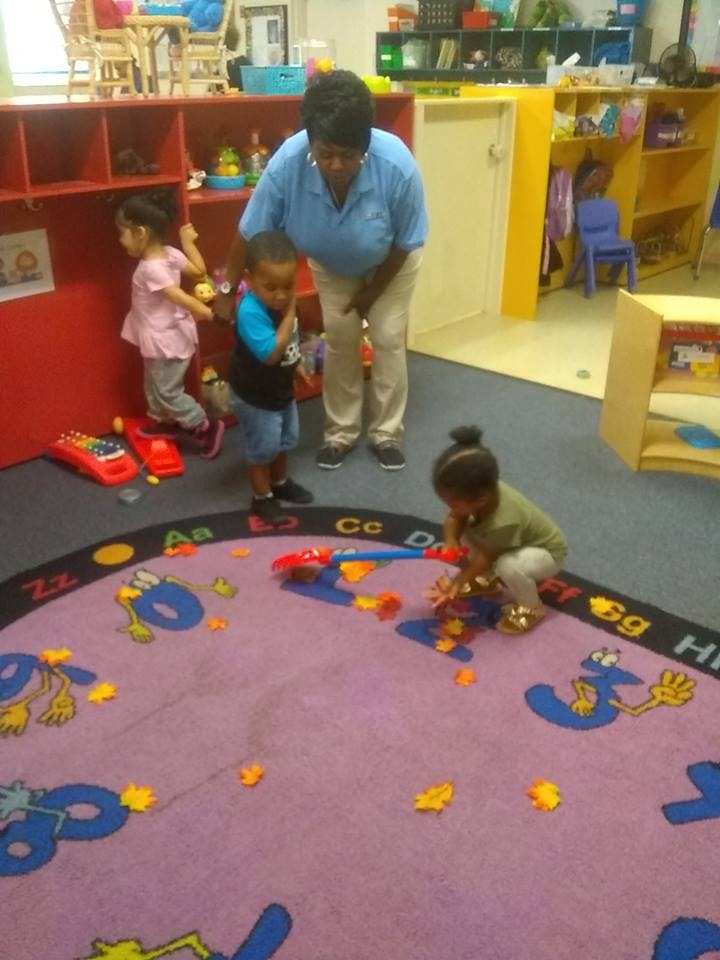 Adult and children playing with toys on a rug in a classroom