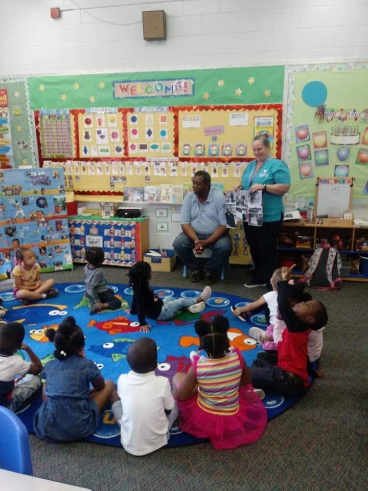 Adults and children sitting on a rug in a classroom