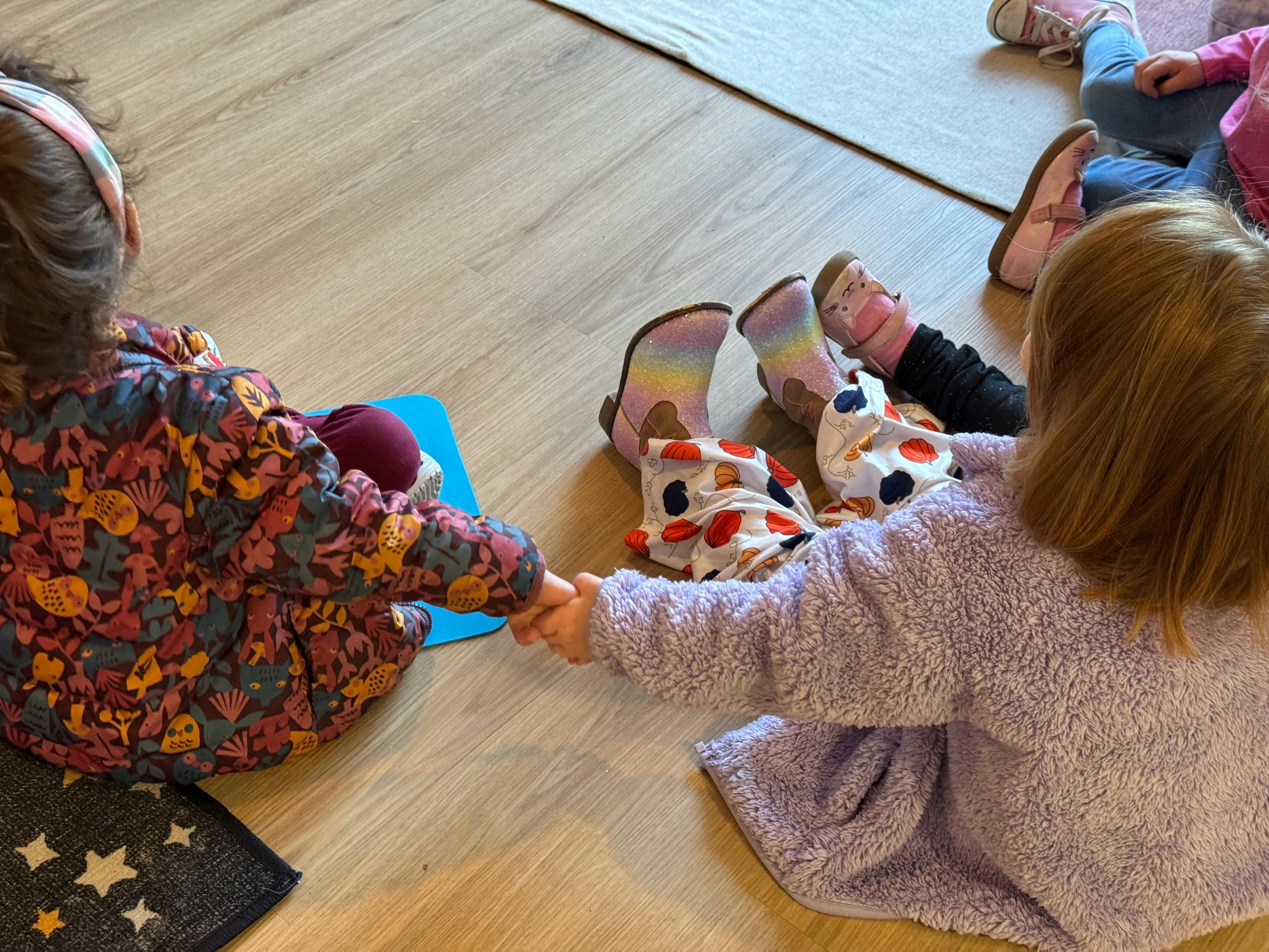 Two children sitting on the floor holding hands