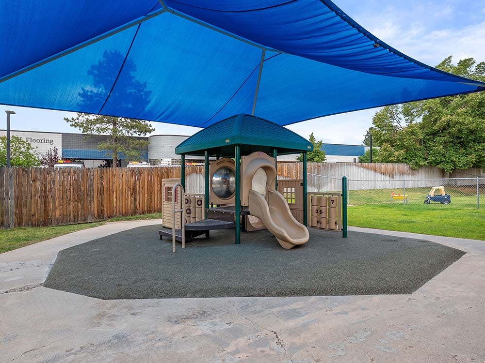 A playground with a slide and climbing structure under a blue shade covering