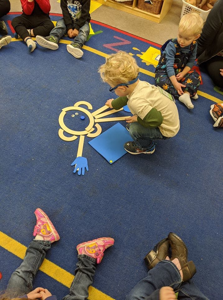 Child playing with craft sticks and paper on a blue rug