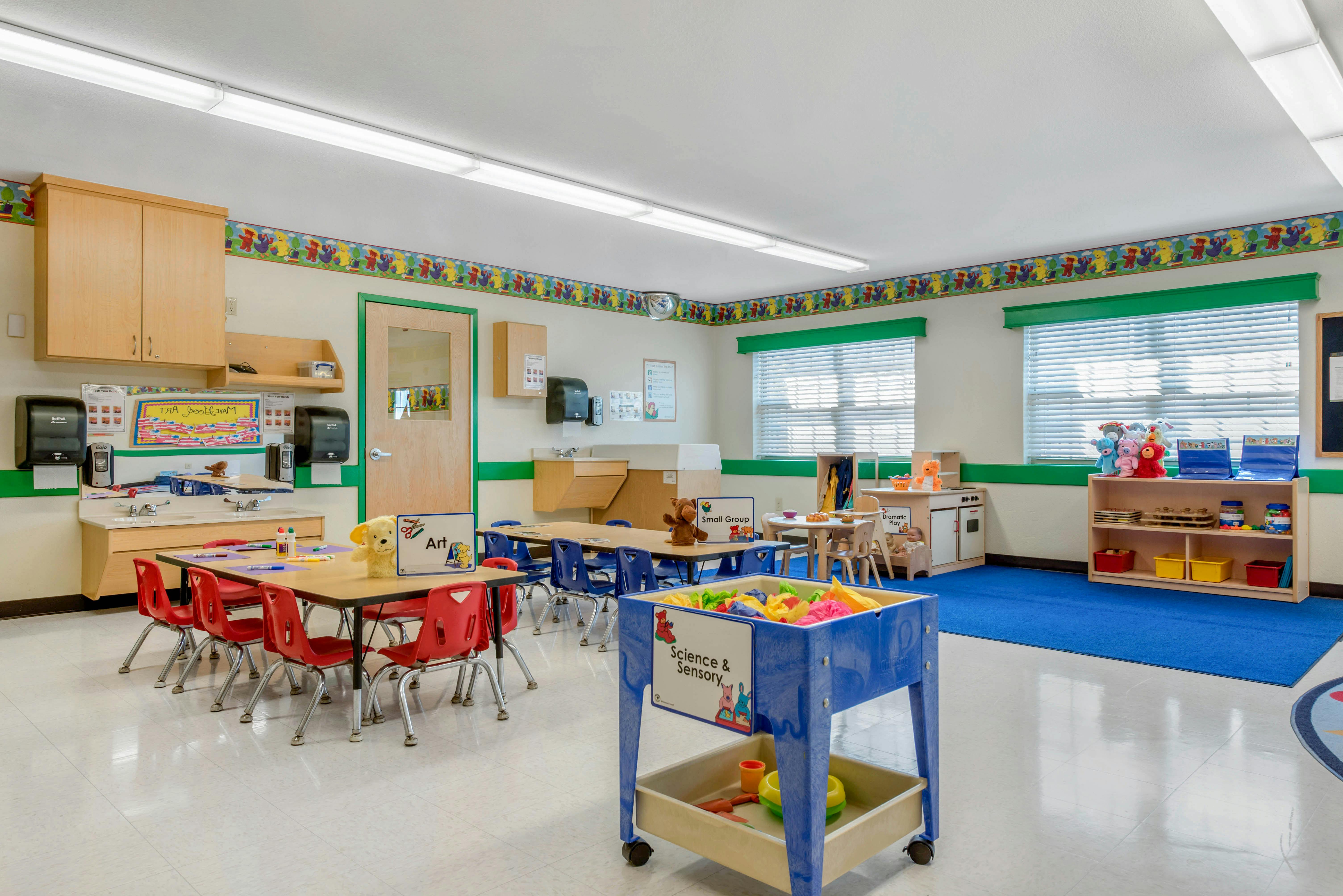 A colorful empty classroom with small tables, chairs, and play areas