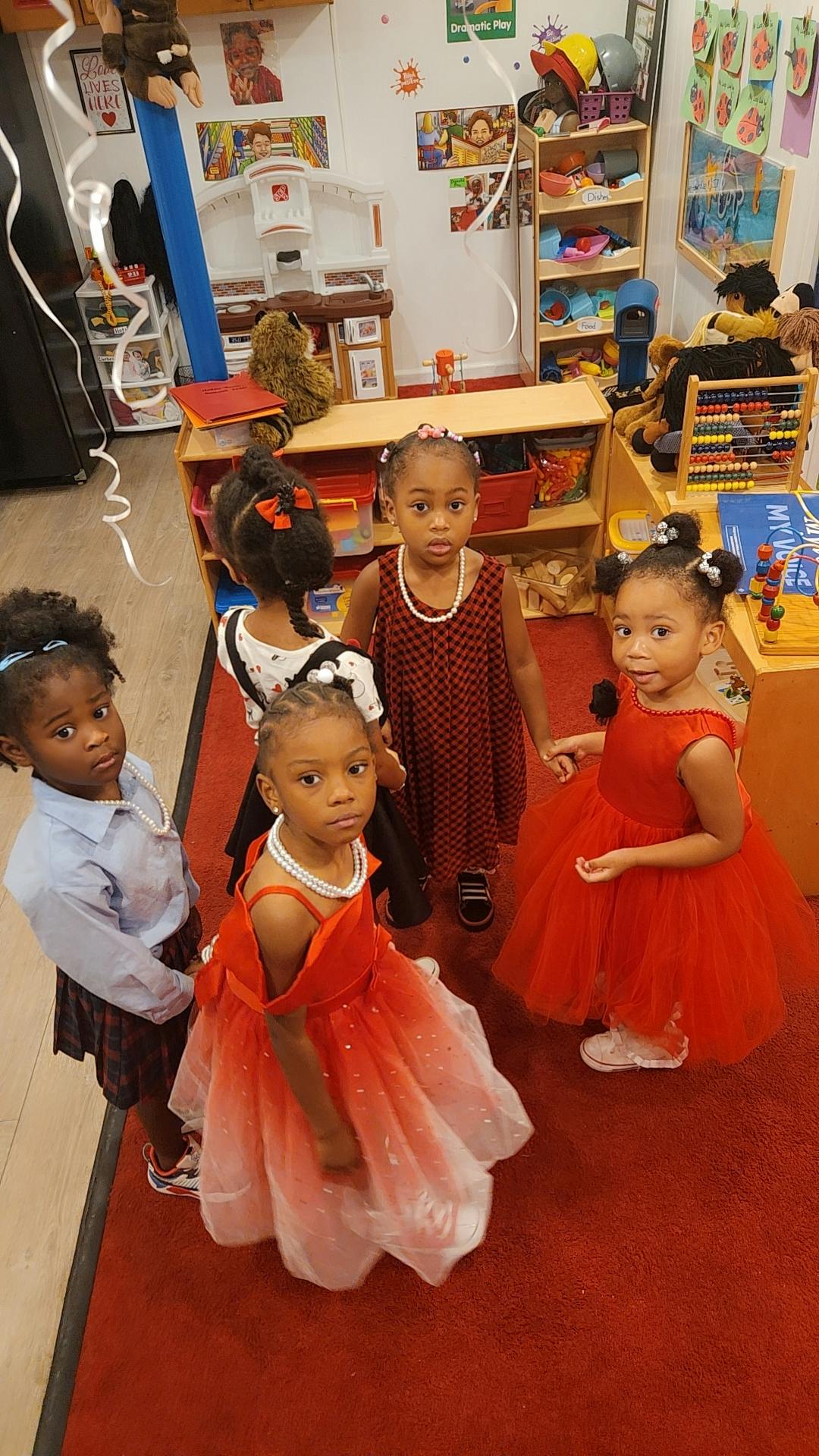 Four children in a classroom, two wearing red dresses
