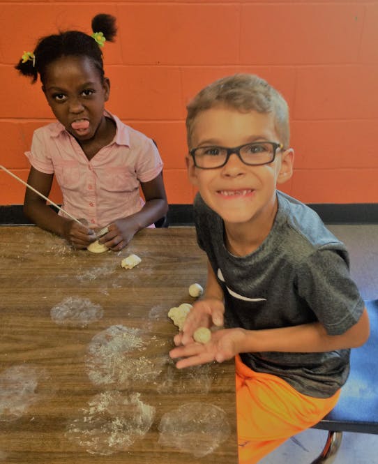 Two children making dough balls at a table