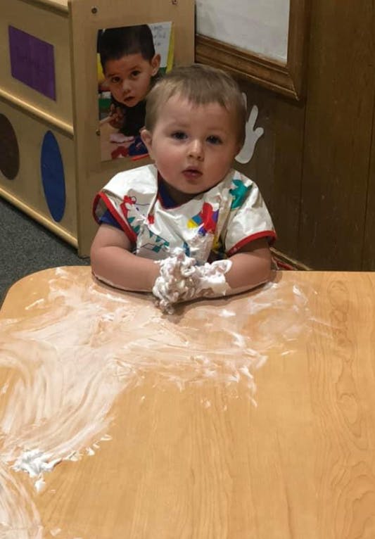 Child in a bib with hands covered in white foam at a table