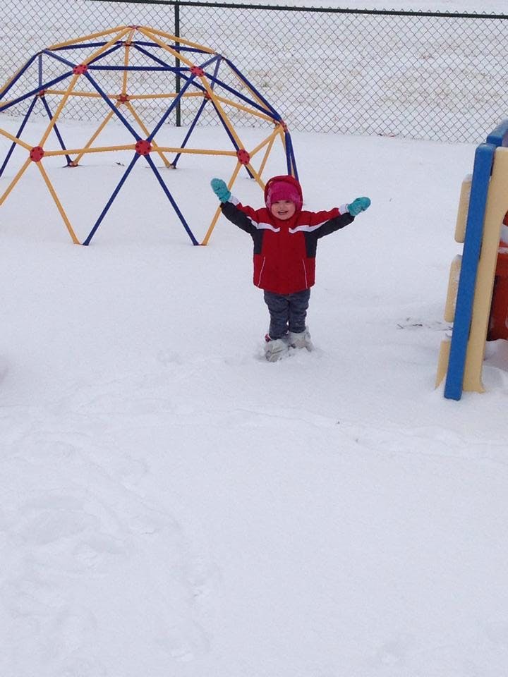 Child in red coat and hat standing in snow with arms outstretched