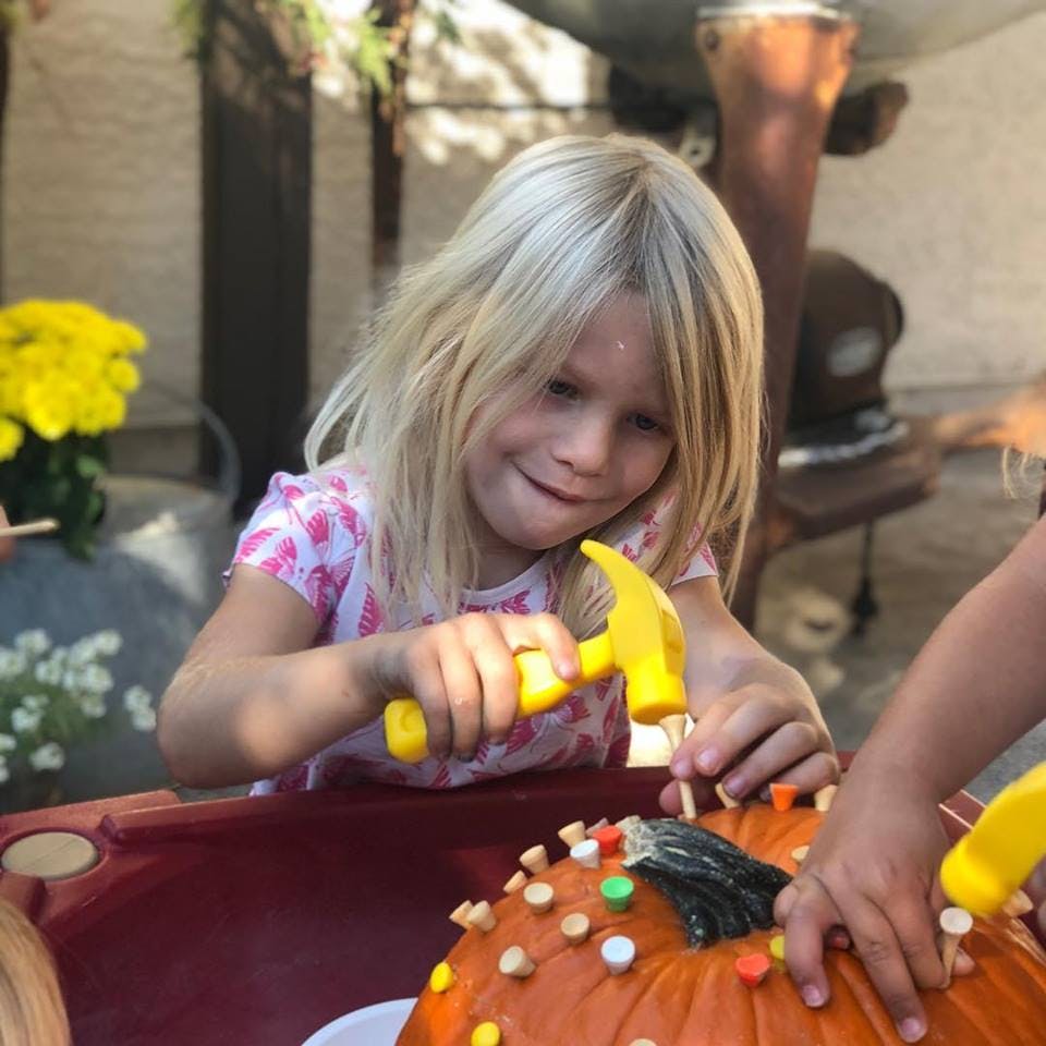 Child using a toy hammer to decorate a pumpkin