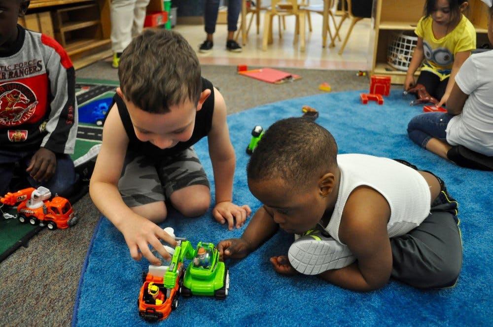 Two children playing with toy trucks on a blue rug