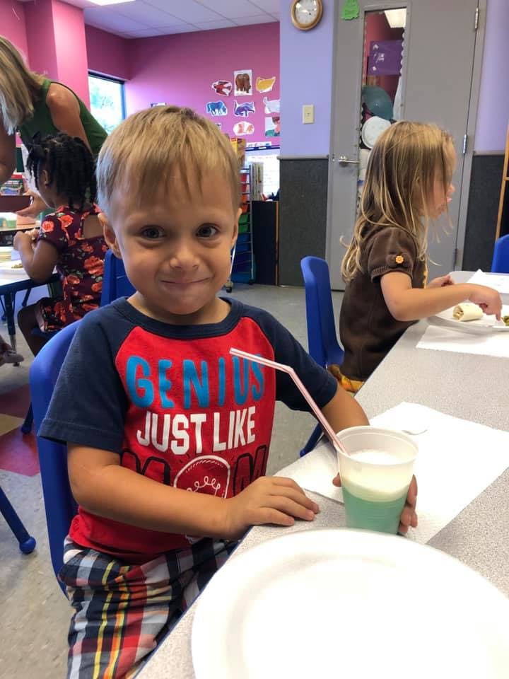 Child in a classroom with a drink and a plate