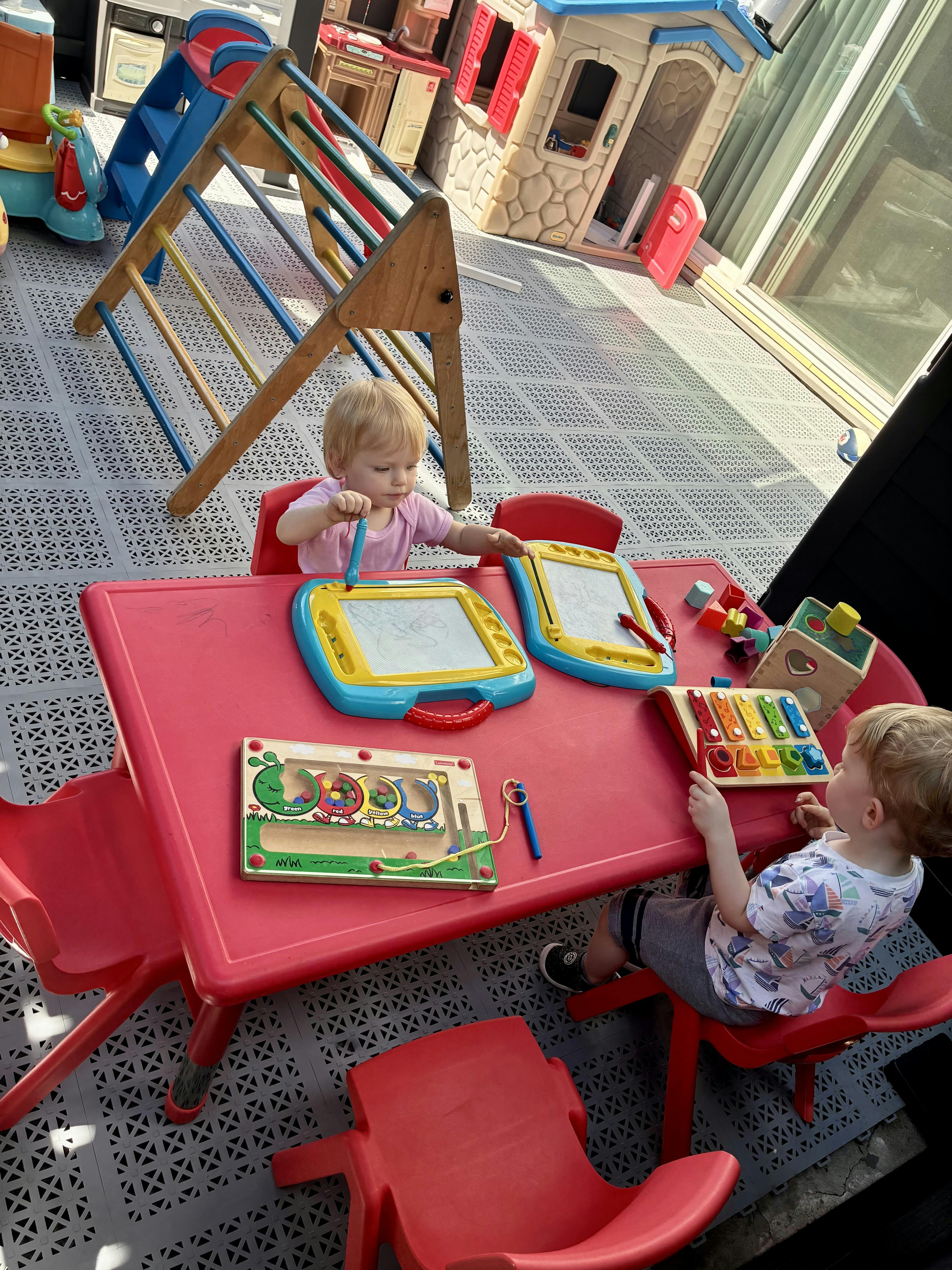 Two children playing with toys at a red table outdoors
