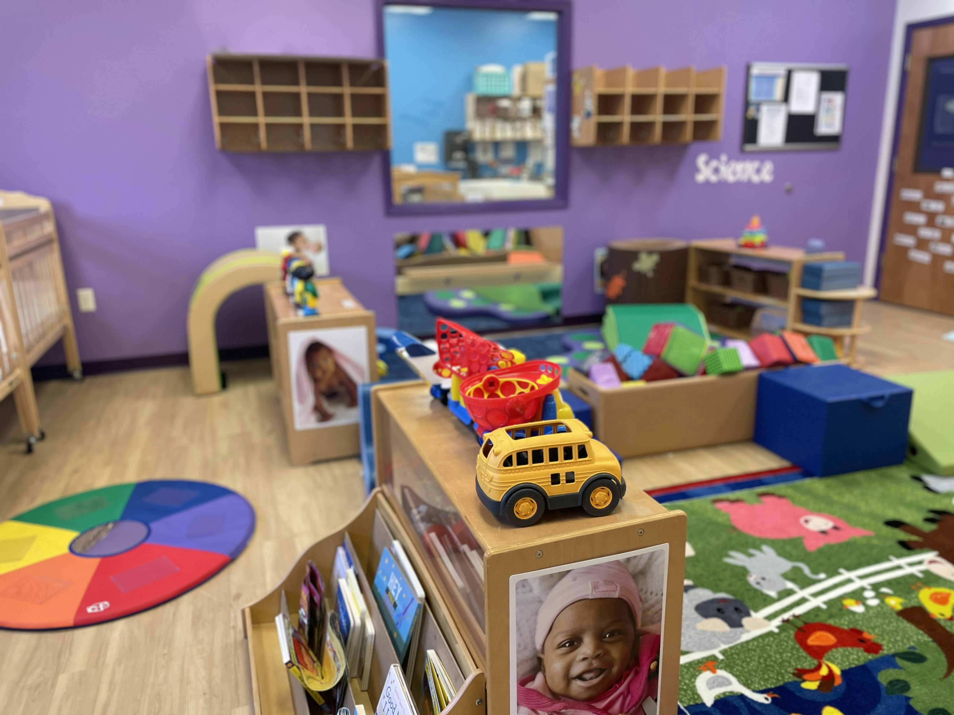 A playroom with purple walls, a circular rainbow mat, and a toy school bus