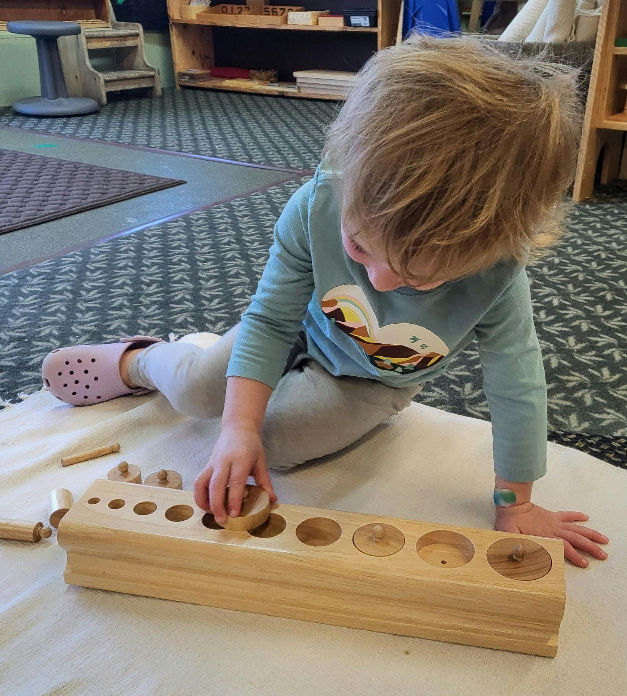 Child playing with a wooden cylinder block puzzle