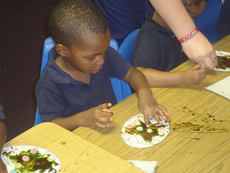 Child decorating a paper plate with an adult's hand assisting
